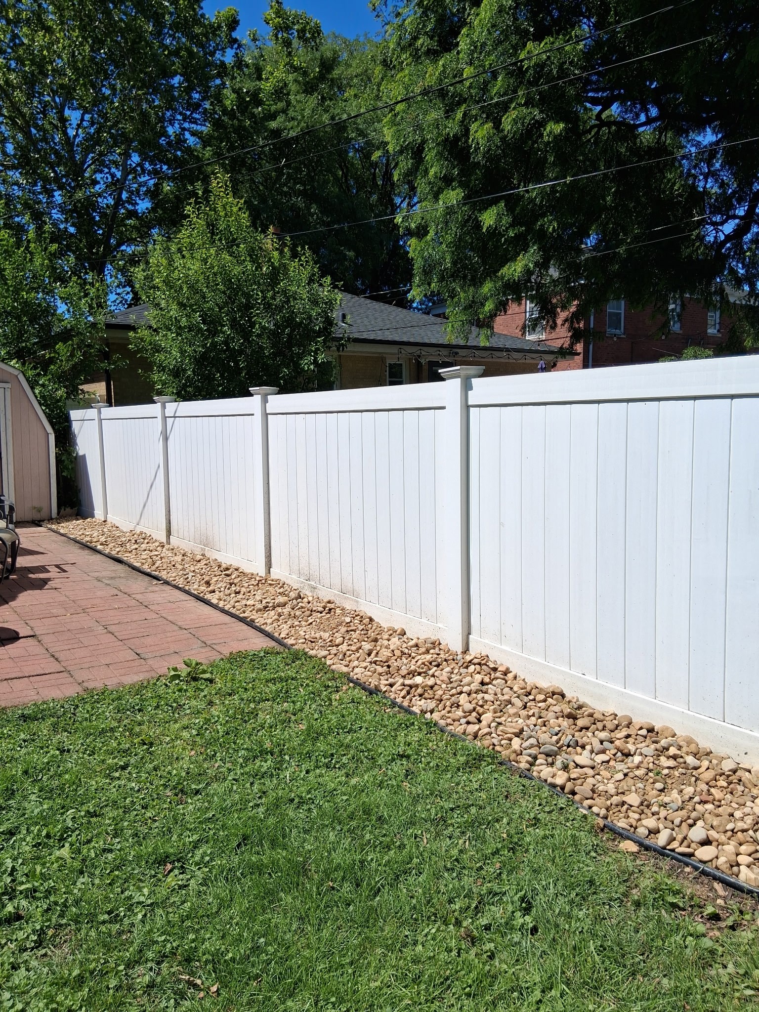 A clean river-rock drainage bed installed along a white vinyl fence by AJ Landscaping